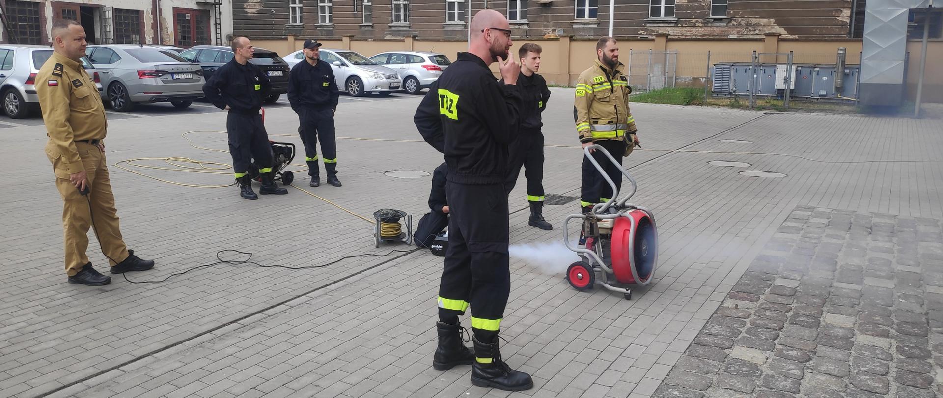 Na zdjęciu strażacy sprawdzają kształt strumienia powietrza przy pomocy zadymiarki