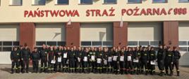 Absolwenci Szkolenia Podstawowego Strażaków Ratowników OSP na pamiątkowym zdjęciu wraz z kadrą dydaktyczną na tle budynku KP PSP Środa Wlkp.