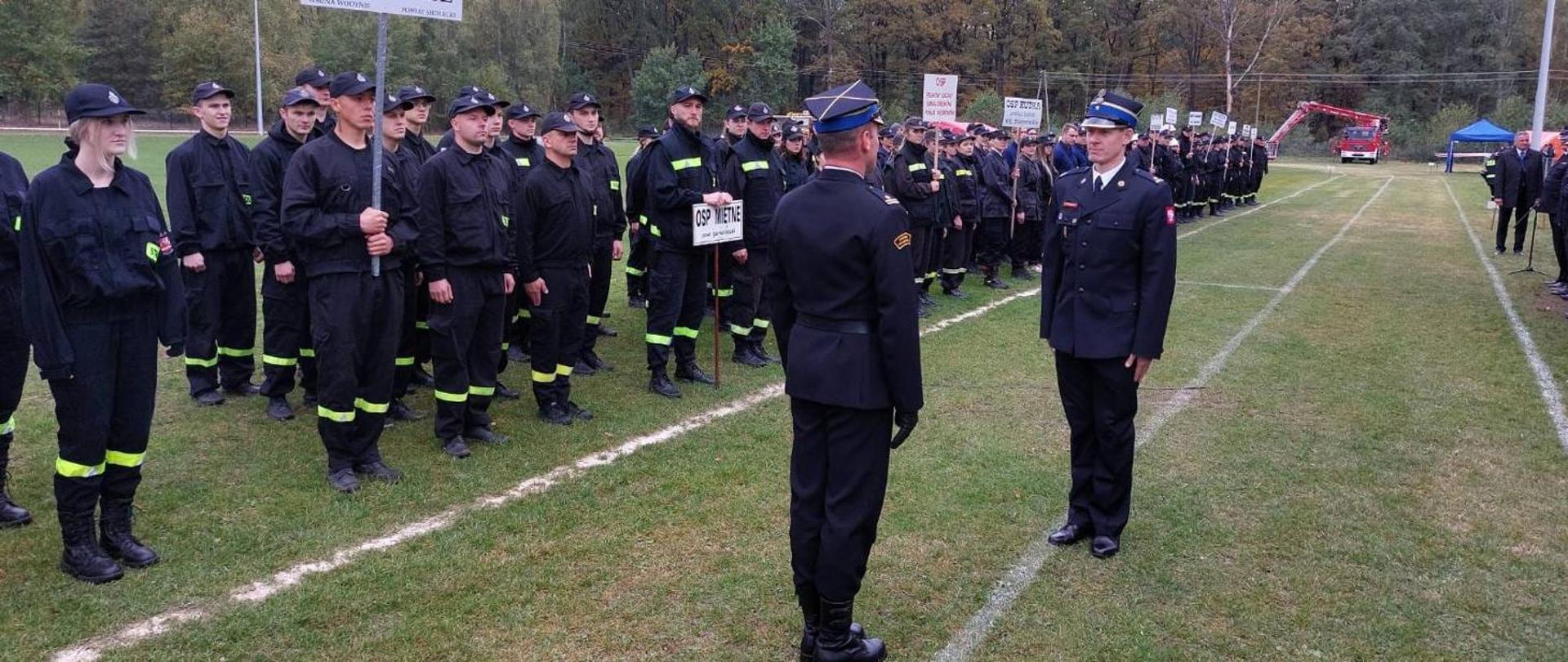 Eliminacje strefowe do VII Wojewódzkich Zawodów Sportowo-Pożarniczych OSP w Pilawie - na zdjęciu strażacy w ubraniu koszarowym stoją w szeregu na zbiórce na boisku trawiastym.