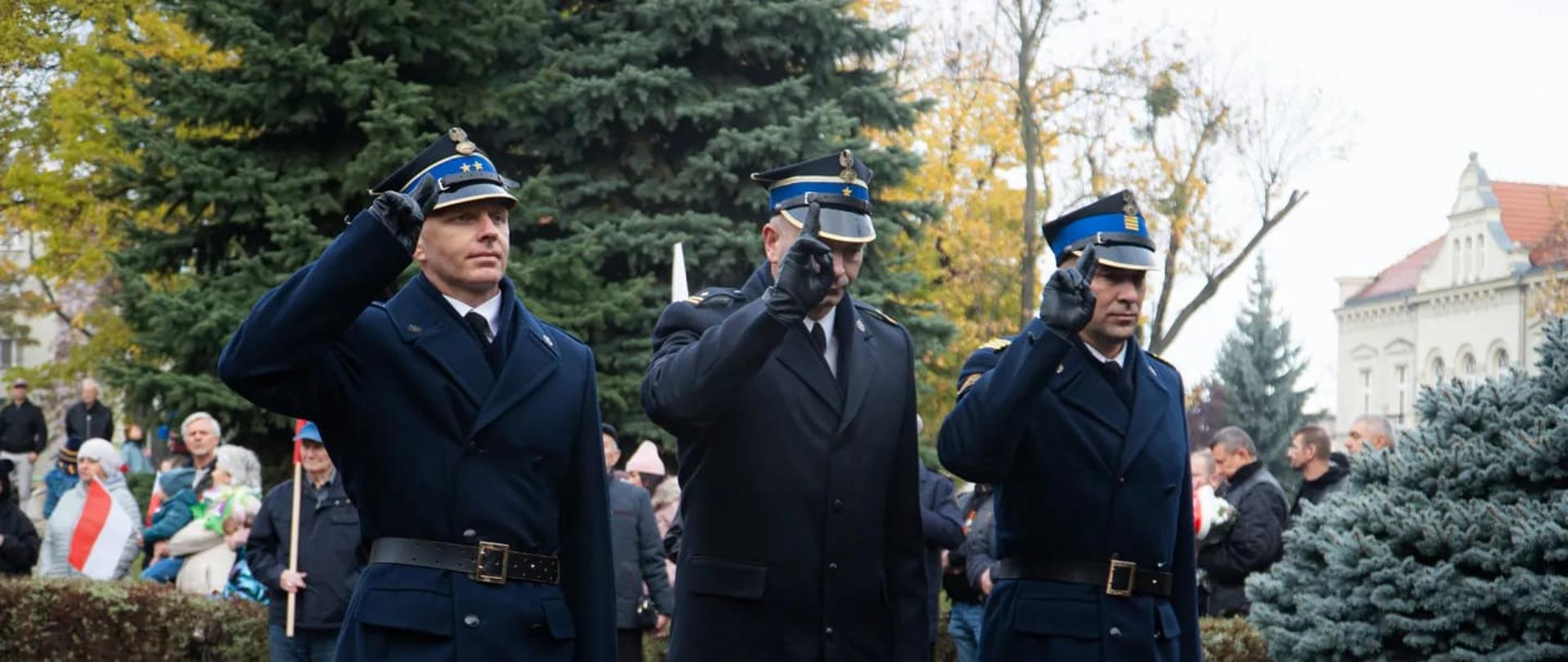 Strażacy w umundurowaniu wyjściowym oddający honory podczas zbbiórki..