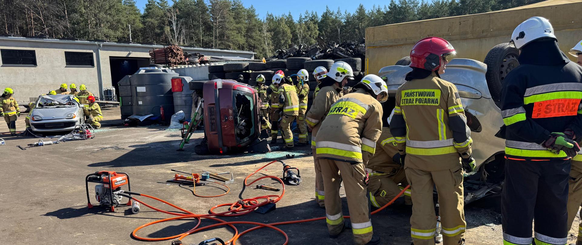 Trzy stanowiska ćwiczebne. Na jednym wrak samochodu znajduje się w pozycji na kołach, na drugim na boku, na trzecim na dachu. Obok wraków stoją druhowie i stabilizują pojazdy.