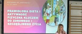 Przed ekranem, na którym wyświetlono slajd prezentacji, stoi kobieta prowadząca wykład, mówi do mikrofonu