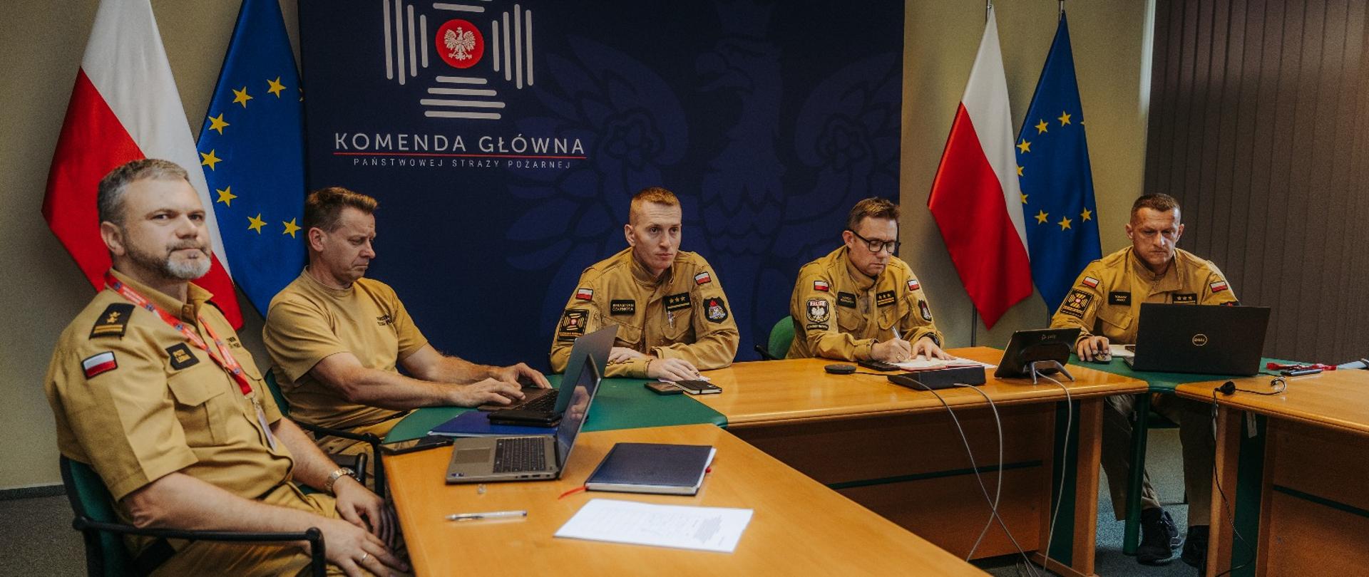 Zespół strażaków PSP w sali konferencyjnej Komendy Głównej PSP podczas odprawy sztabowej. Na stole laptopy i dokumenty, w tle tablica z logotypem PSP oraz flagi Polski i Unii Europejskiej.
Moduł MSO7