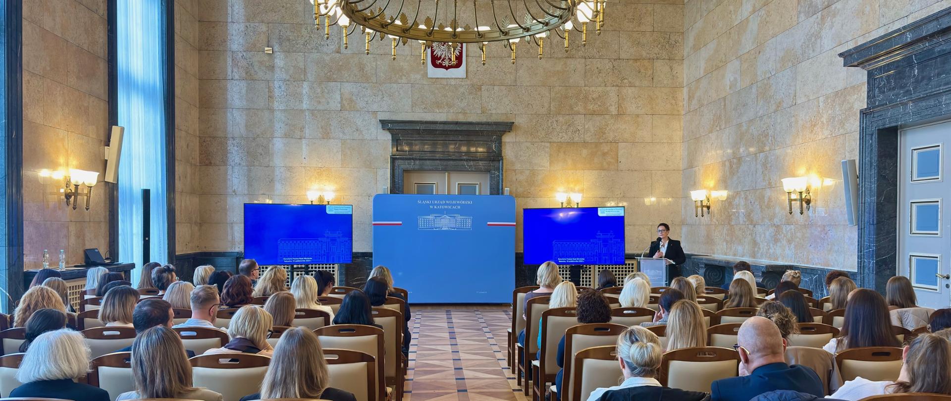 Szefowa służby cywilnej w Śląskim Urzędzie Wojewódzkim - przemawia przy mównicy w marmurowej sali z dużym żyrandolem
