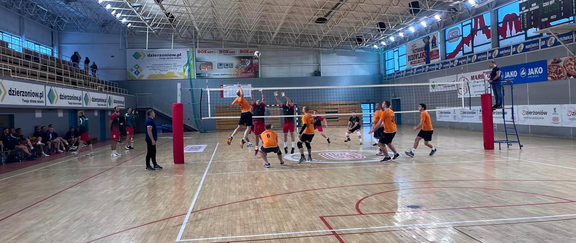 Funkcjonariusze grając w piłkę siatkową na hali sportowej.