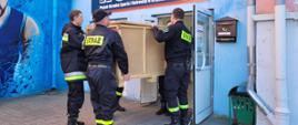 Strażacy PSP i OSP wnoszą skrzynię przez drzwi do hali MOSIR.