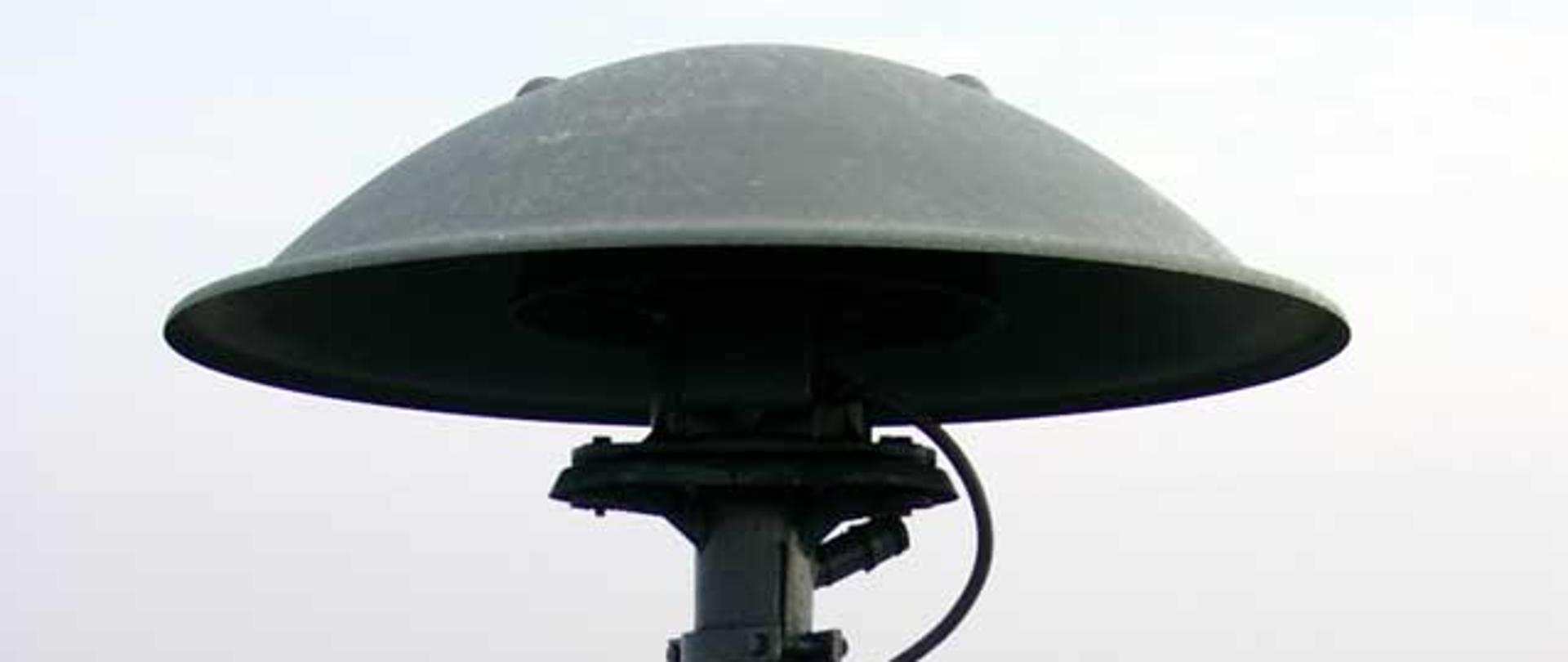 Na zdjęciu syrena alarmowa, W tle pejzaż miasta. 