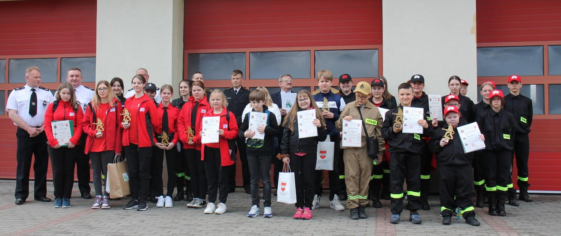 przed bramami garażowymi PSP stoją w dwuszeregu ustawieni laureaci tegorocznej edycji OTWP trzymając w ręku dyplomy