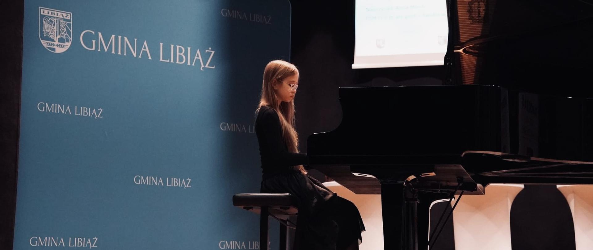 Dziewczynka gra na fortepianie na estradzie, w tle baner z napisem Gmina Libiąż.