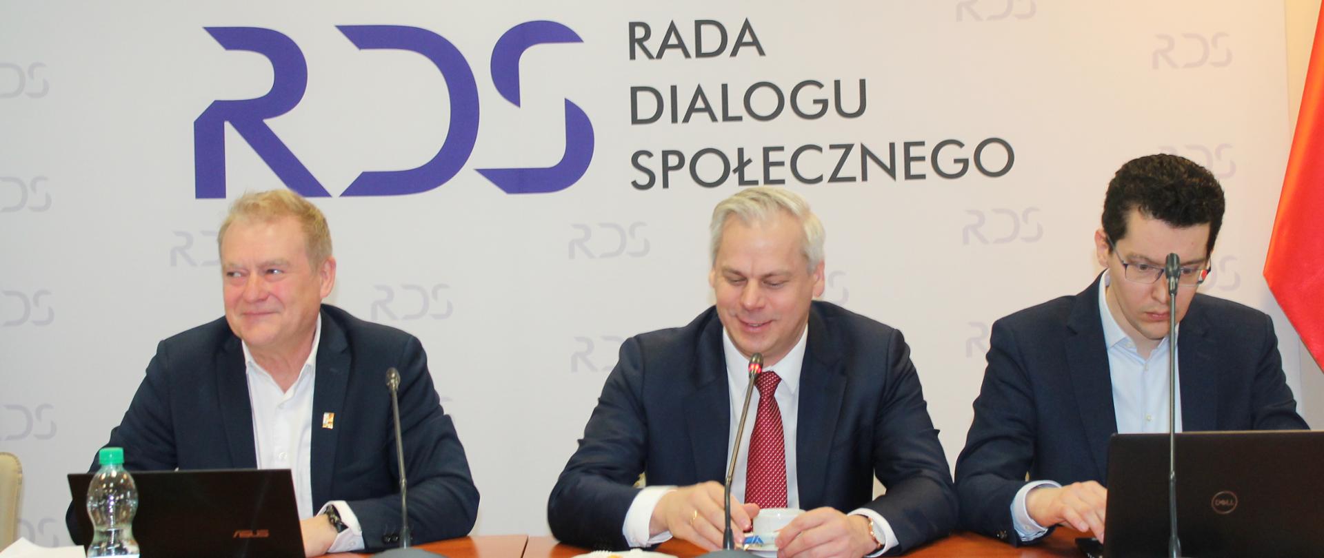 Zdjęcie przedstawia stół prezydialny, za którym siedzą: Pan Krzysztof Kisielewski, Współprzewodniczący Zespołu ze strony związków zawodowych, Pan Karol Rabenda, Podsekretarz Stanu w Ministerstwie Aktywów Państwowych oraz Pan Marcin Izdebski, Dyrektor Departamentu Spółek Paliwowo-Energetycznych w Ministerstwie Aktywów Państwowych. W tle znajduje się baner z napisem Rada Dialogu Społecznego.