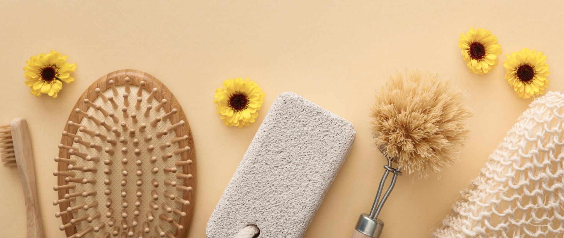 Na zdjęciu jest szczoteczka do zębów, szczotka do włosów, pumeks oraz gąbka. Tło jest beżowe.