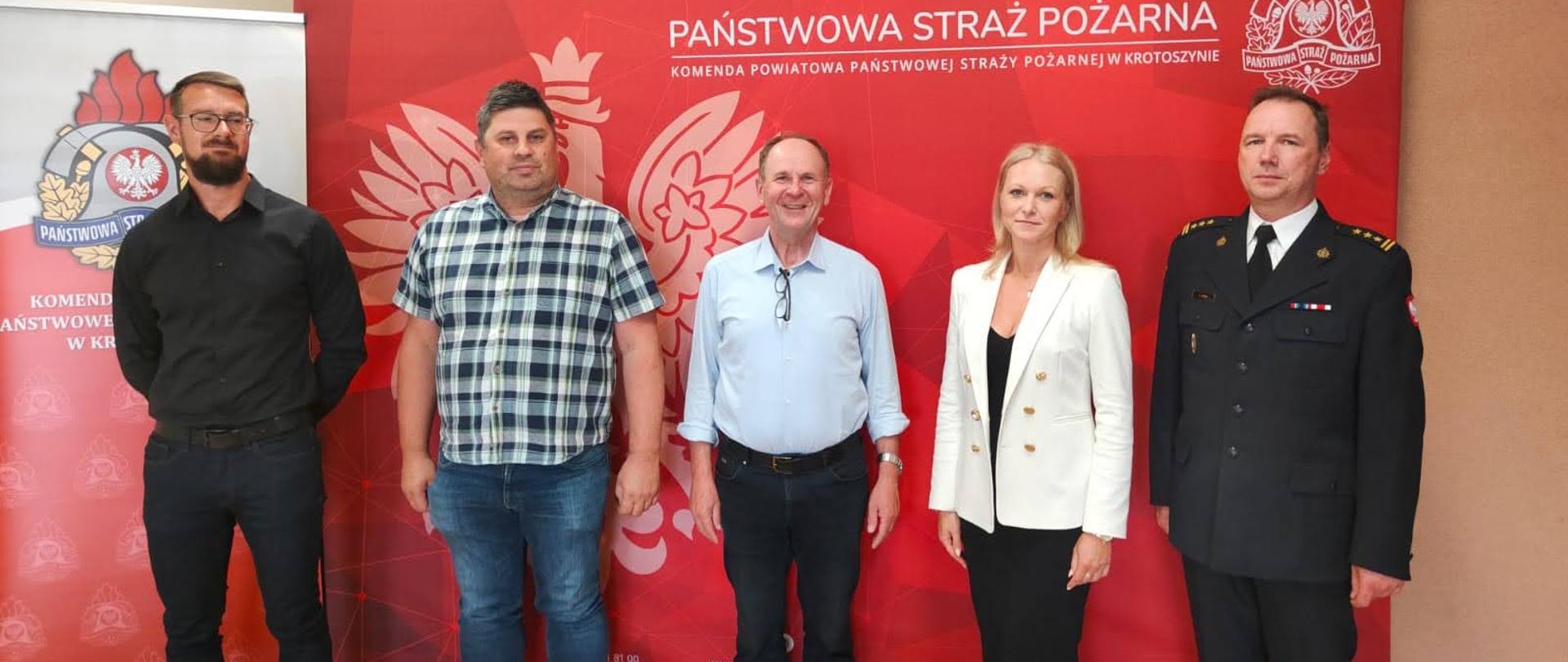 Na świetlicy komendy powiatowej, st. bryg. Marek Kalak składa na ręce lokalnych przedsiębiorców podziękowania za wsparcie finansowe. Zdjęcie grupowe wykonane na tle baneru komendy powiatowego PSP w Krotoszynie