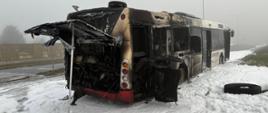 Autobus stojący na jezdni, który uległ spaleniu. Na jezdni piana gaśnicza