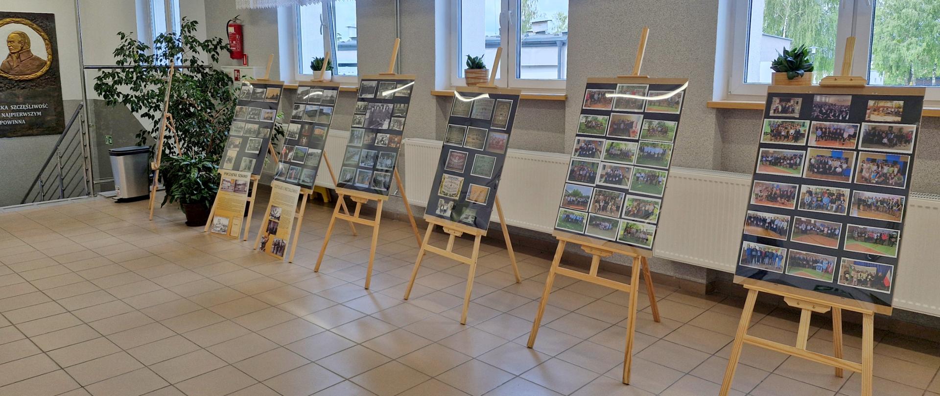 Wystawa zdjęć umieszczonych na sztalugach stojących na szkolnym korytarzu.
