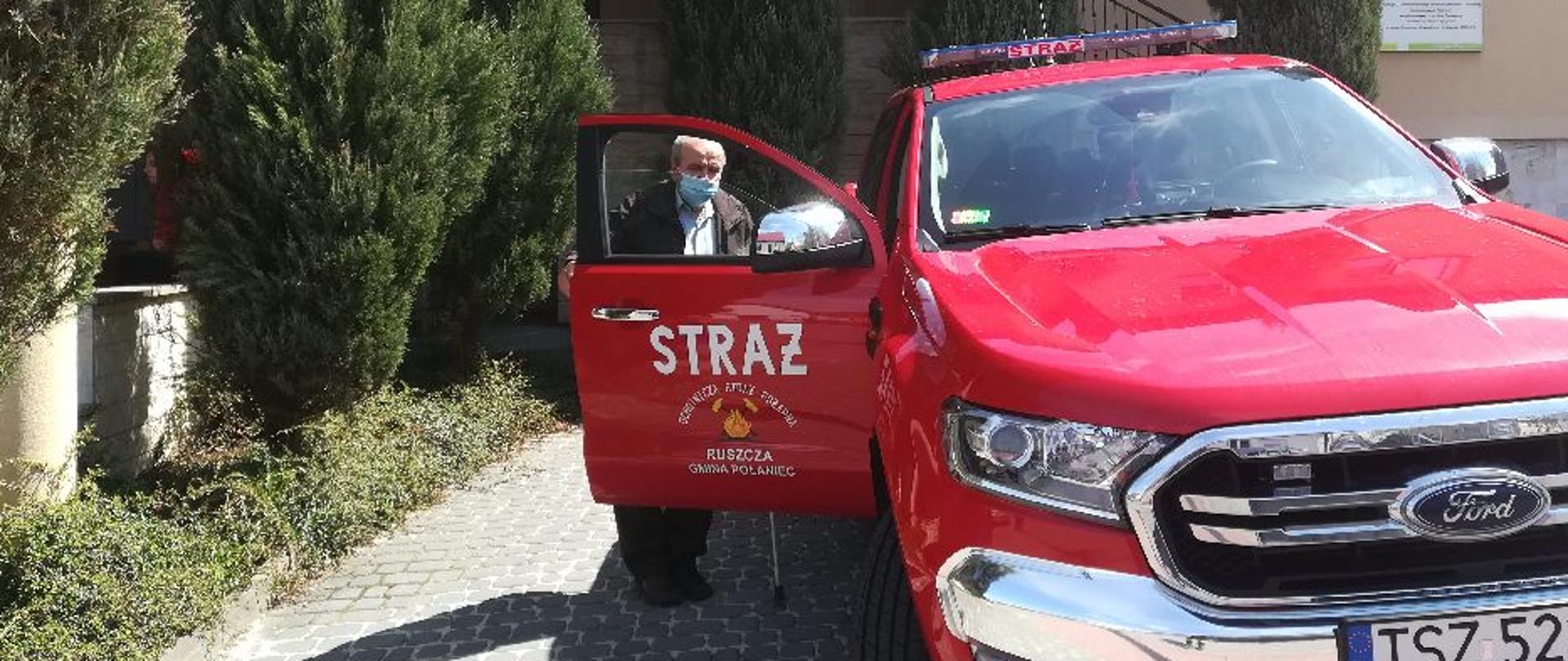 Starsza osoba wsiada do samochodu strażackiego, który znajduje się obok punktu szczepień.