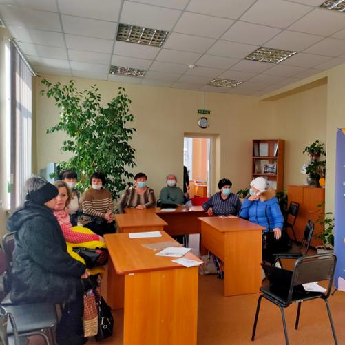 Kilka osób w kurtkach siedzi przy biurkach.