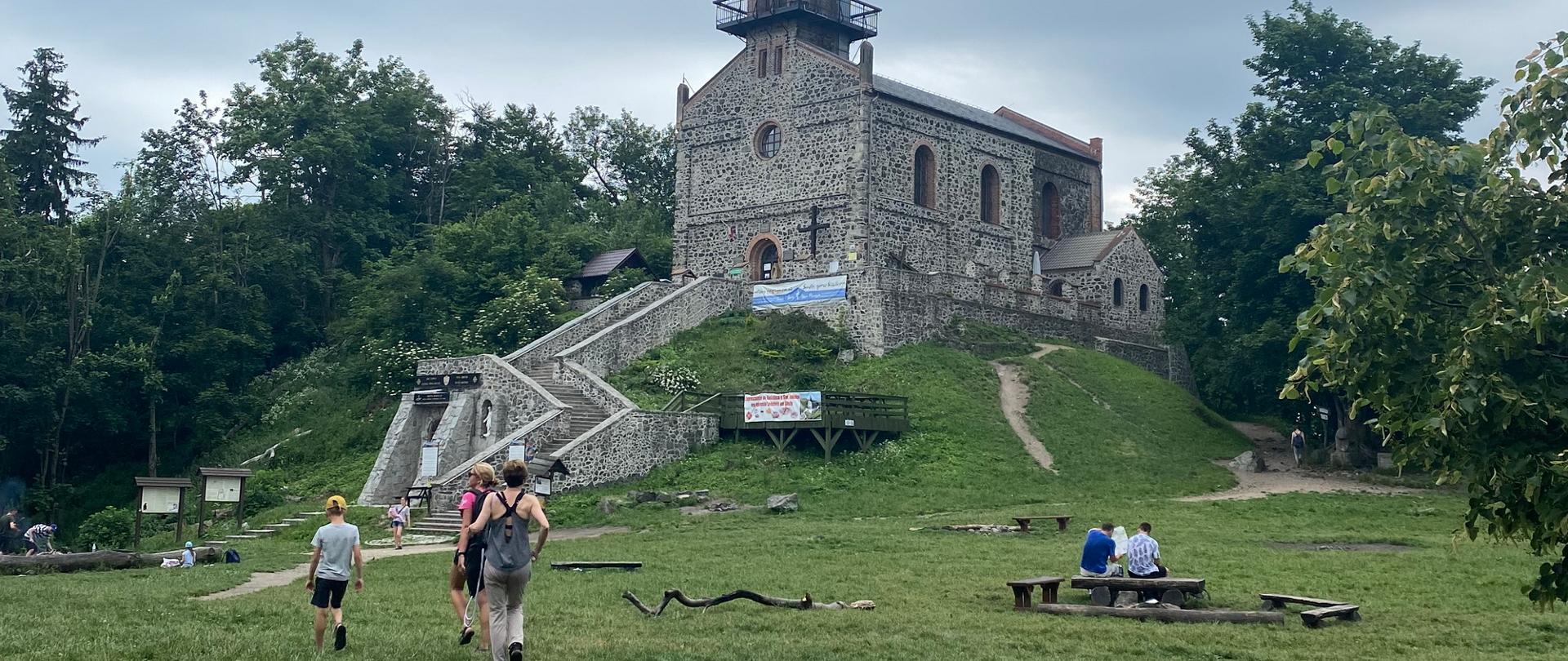 Grupa młodzieży zbliża się do zabytkowego budynku, wokół którego widoczne są drzewa