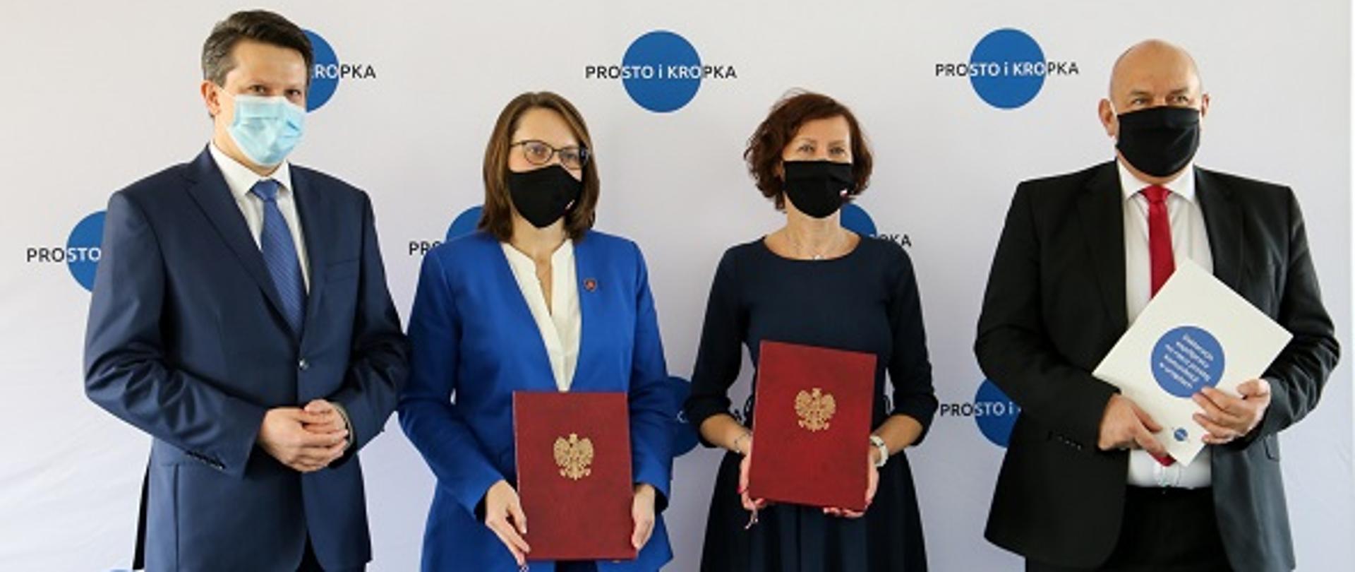 Cztery osoby stoją na tle ścianki z napisem "Prosto i kropka". Są to Marek Redźko, dyrektor generalny MFiPR, szefowa KAS Magdalena Rzeczkowska , Renata Oszast, dyrektor generalna MF oraz minister Tadeusz Kościński