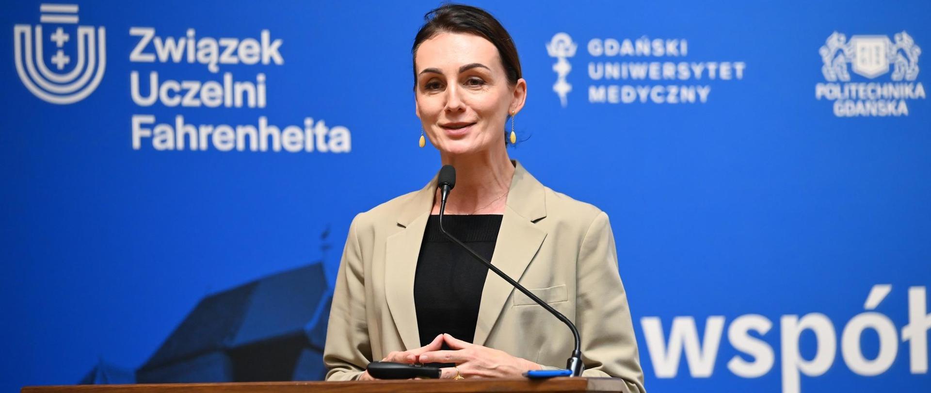 Kobieta (wojewoda) stoi przy mównicy, w tle napis związek uczelni Fahrenheita