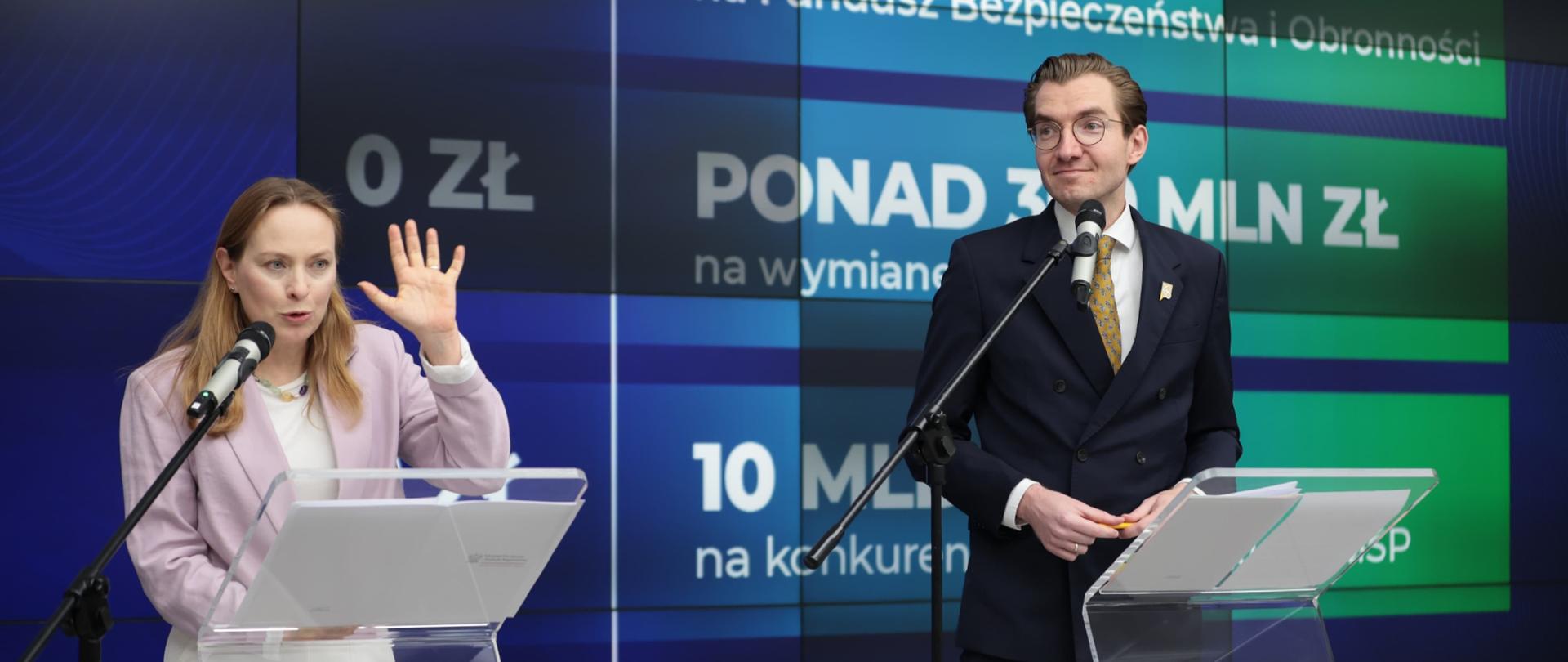 W sali konferencyjnej w mównicach stoją minister Katarzyna Pełczyńska-Nałęcz oraz wiceminister Jan Szyszko