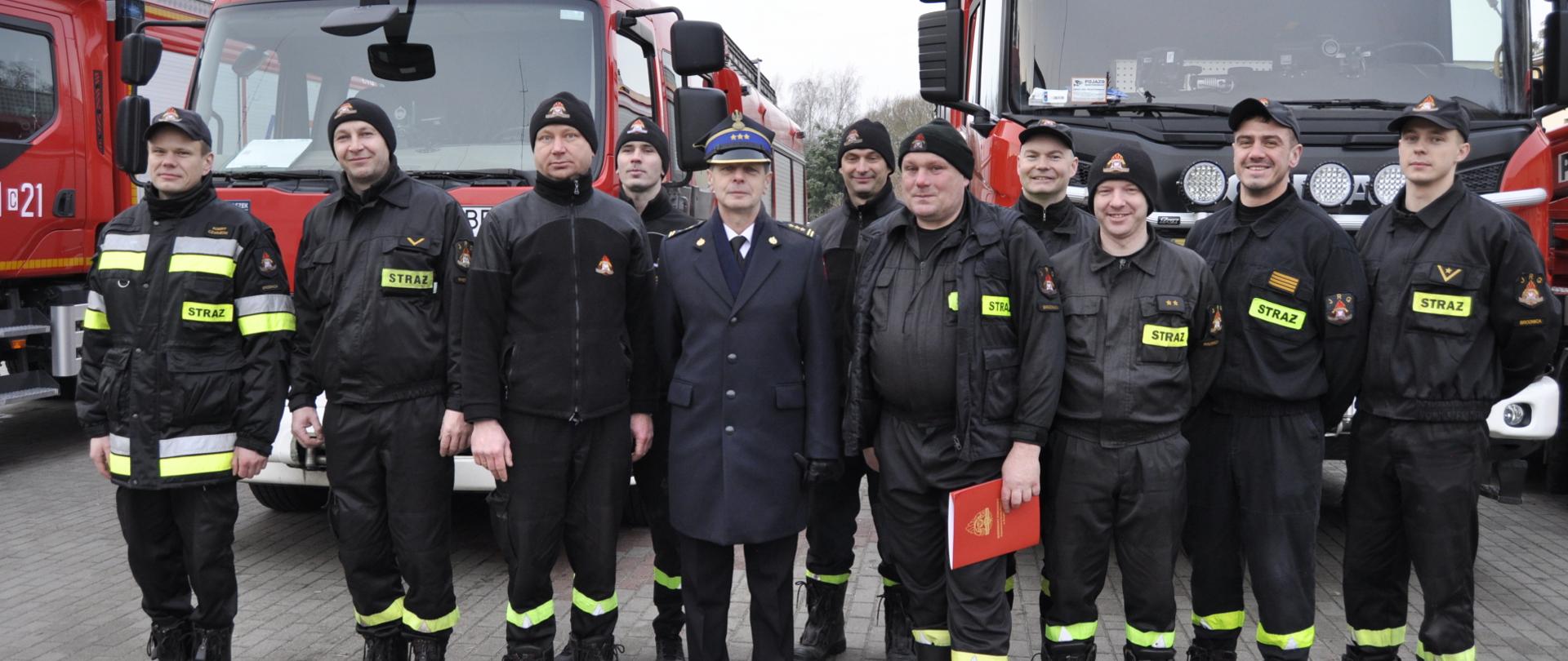 Zdjęcie przedstawia wspólne pamiątkowe zdjęcie st. ogn. Arkadiusza Poniewierskiego z kolegami ze zmiany służbowej JRG w Brodnicy. W tle samochody pożarnicze Komendy. Obok przechodzącego na emeryturę st.bryg.Andrzej Górecki Komendant Powiatowy Państwowej Straży Pożarnej w Brodnicy.