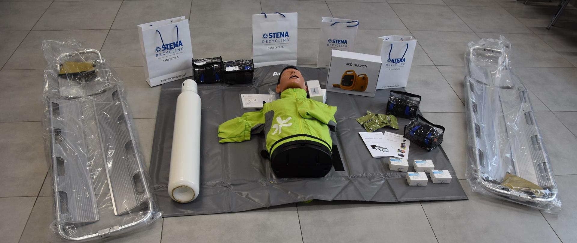 Na zdjęciu widnieje sprzęt ratownictwa medycznego i do szkolenia z tego zakresu np., nosze podbierakowe, butla tlenowa, fantom, defibrylator 