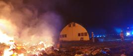 Zdjęcie w porze nocnej. Widać samochody ratowniczo-gaśnicze oraz budynek kurnika. Występuje zadymienie.