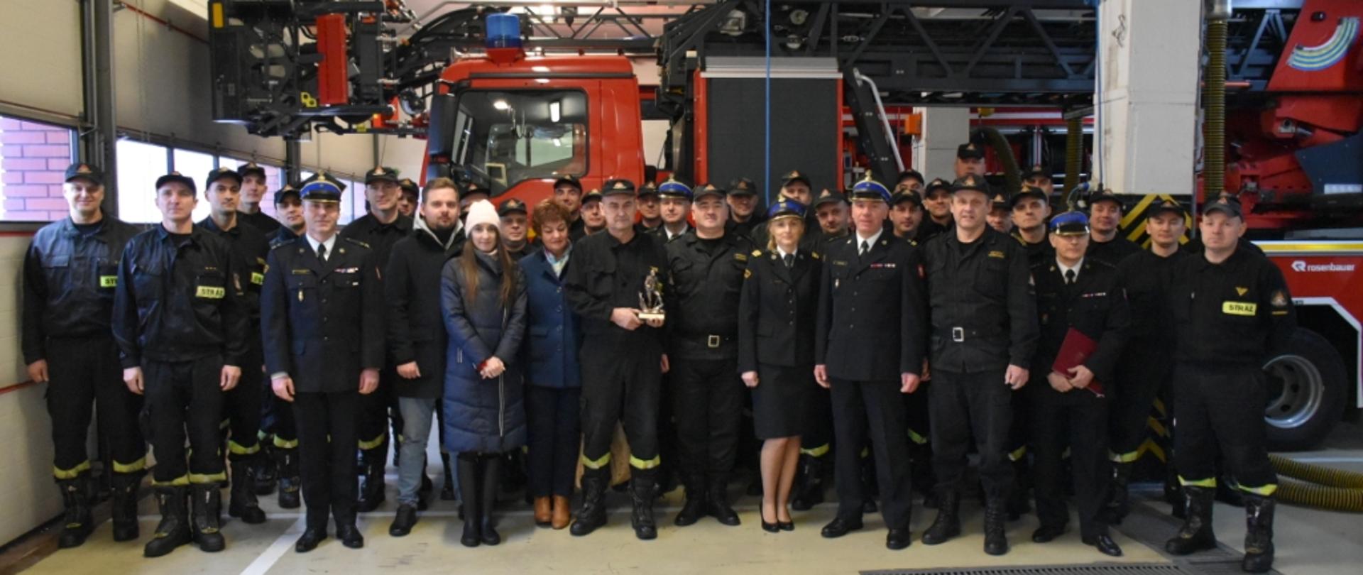 Wspólne zdjęcie pracowników komendy oraz strażaka odchodzącego na emeryturę, idącego w obecności najbliższej rodziny.