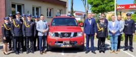 Zdjęcie grupowe zaproszonych gości oraz strażaków przy samochodzie
