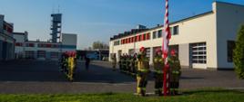 Strażacy PSP w ubraniach specjalnych oraz mundurach wyjściowych na placu Komendy podczas uroczystej zbiórki i podniesienia Flagi Rzeczypospolitej Polskiej z okazji święta 2 maja.