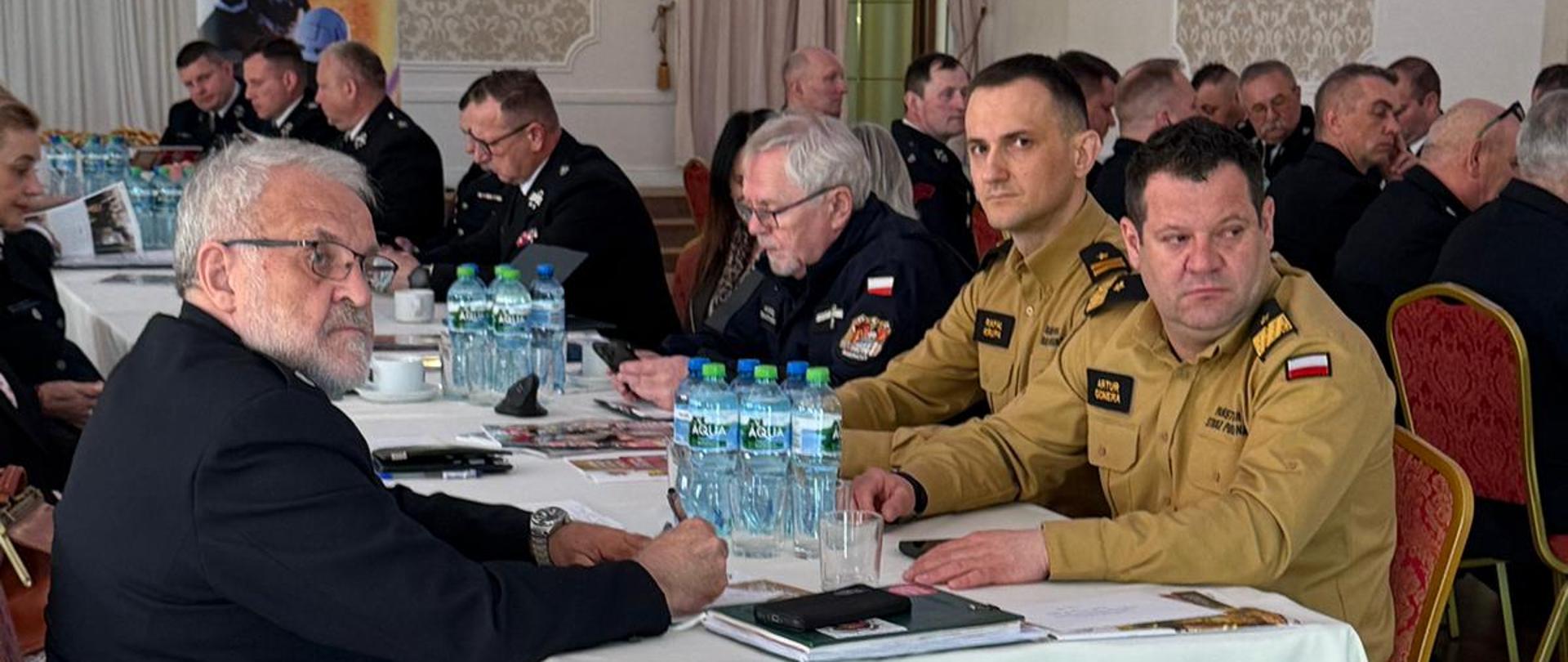 Uczestnicy narady siedzą przy stołach.