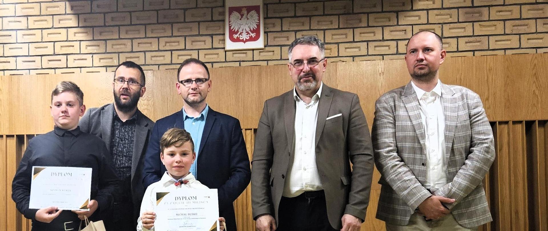 Zdjęcie przedstawiające komisję konkursową, oraz laureatów pozujących do zdjęcia na scenie konkursowej 