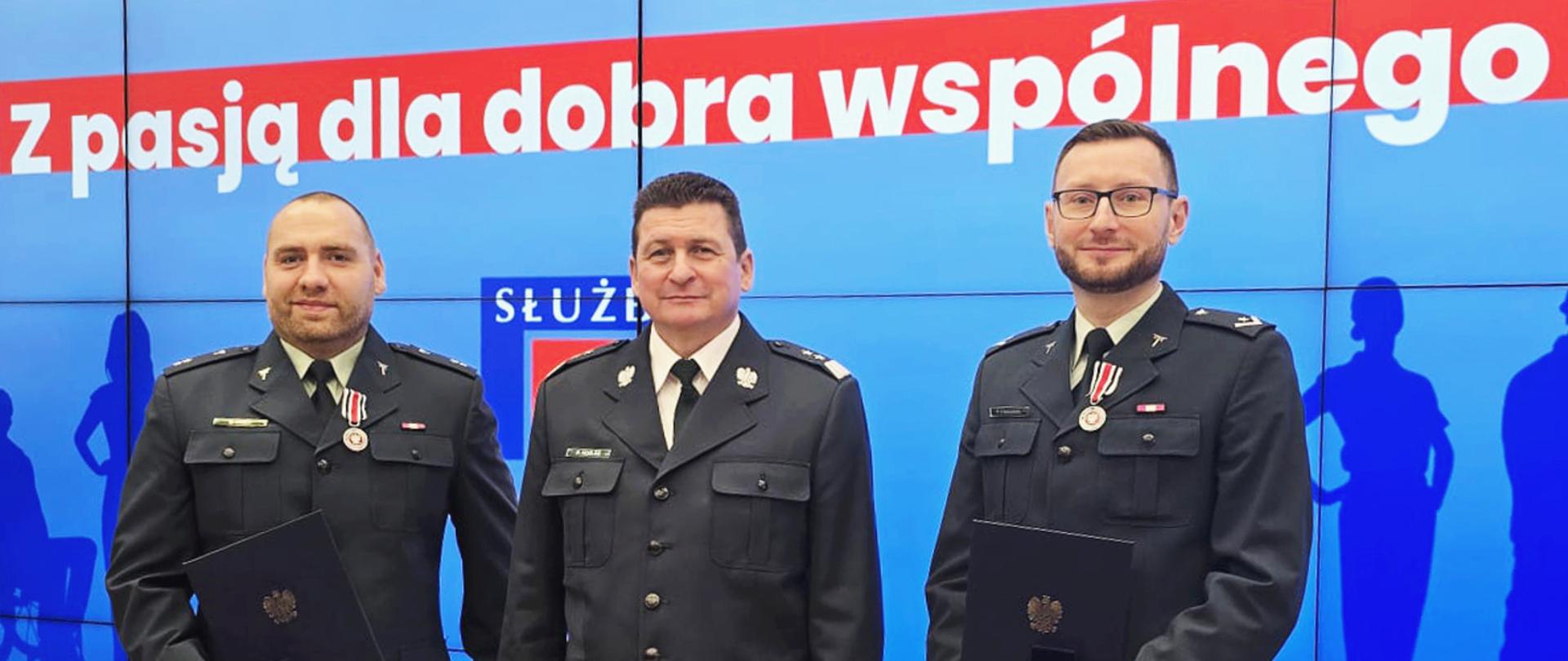 Trzech mężczyzn na tle ekranu z napisem Dzień Służby Cywilnej. W centrum Główny Inspektor, a po lewej i po prawej inspektorzy z przypiętymi odznakami. Mężczyźni są w inspekcyjnym umundurowaniu.