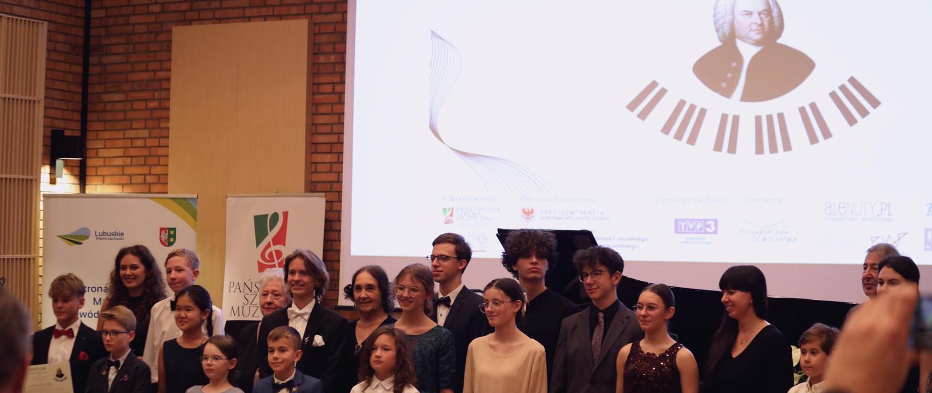 Laureaci i Jury z dyplomami. W tle ekran z grafiką J.S. Bach