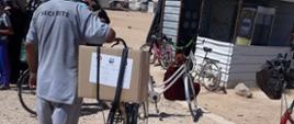 mężczyzna na rowerze wiezie paczkę oznakowaną logo Polska pomoc
