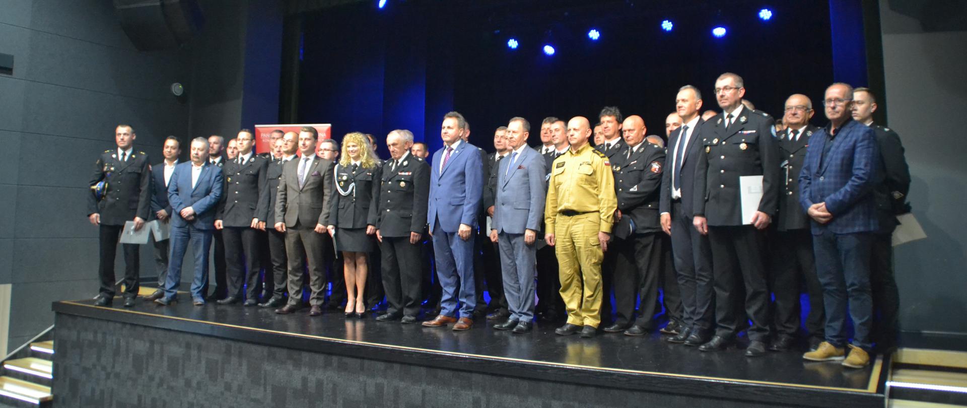 Na zdjęciu znajdują się wszyscy zaproszeni goście oraz wszyscy strażacy ubrani w mundury galowe. Jest to wspólne zdjęcie, wszyscy stoją na scenie Sali widowiskowej domu kultury Śnieżka w Dębicy.