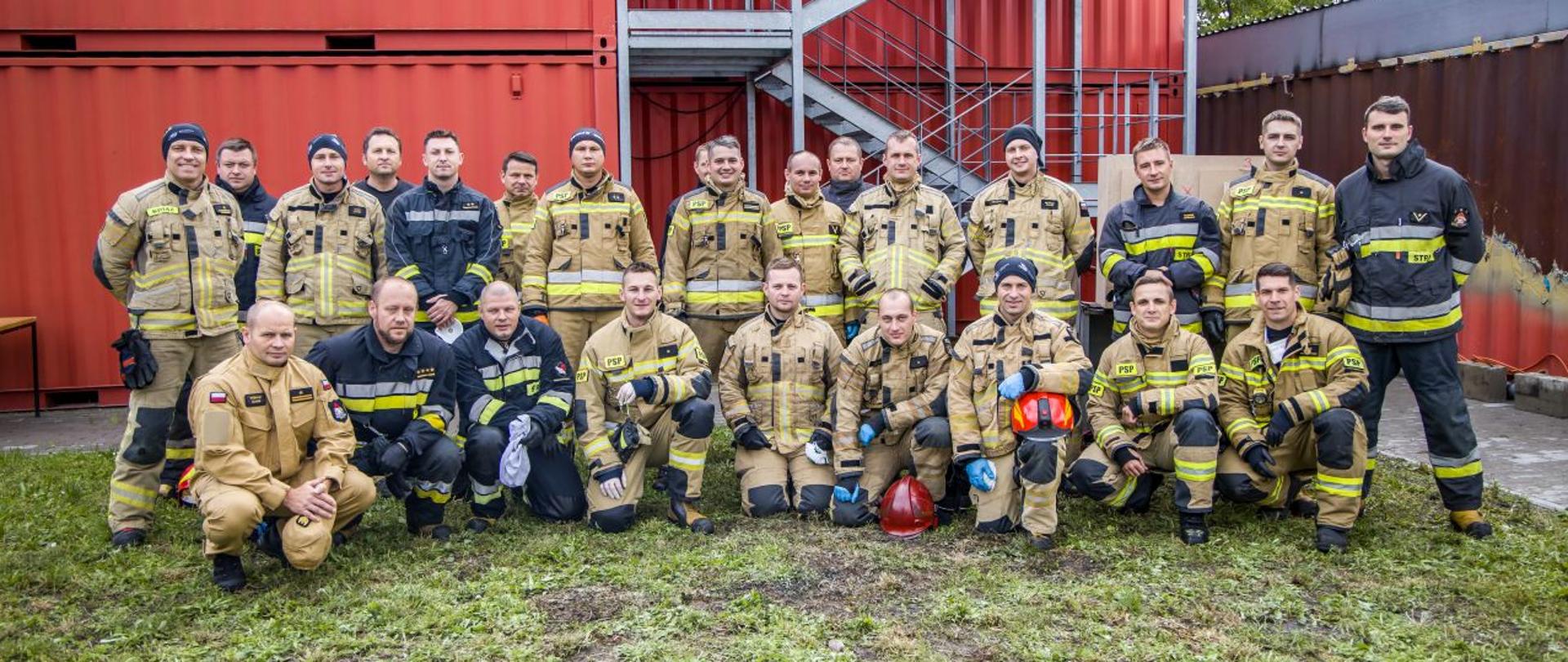Strażacy podczas części praktycznej szkolenia z zakresu gaszenia pożarów wewnętrznych - wspólne zdjęcie uczestników oraz instruktorów kursu