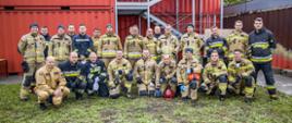 Strażacy podczas części praktycznej szkolenia z zakresu gaszenia pożarów wewnętrznych - wspólne zdjęcie uczestników oraz instruktorów kursu