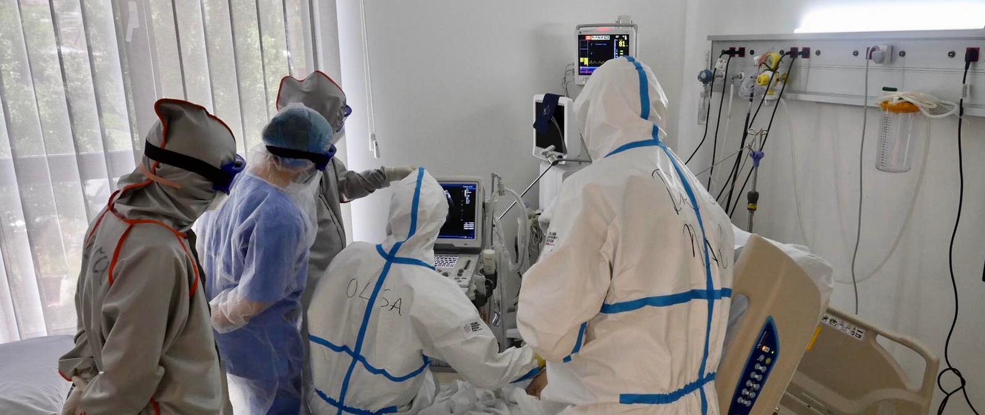 grupa lekarzy ubranych w kombinezony nad pacjentem