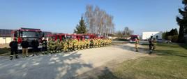 Strażacy stoją w szeregu przed wozem strażackim, gotowi do rozpoczęcia ćwiczeń.