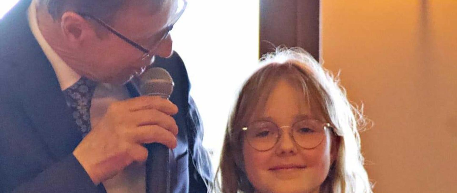 Burmistrz miasta Szczytna stoi wraz Natalią Skrzydłom, która trzyma bon na kwotę pieniężną 500 zł