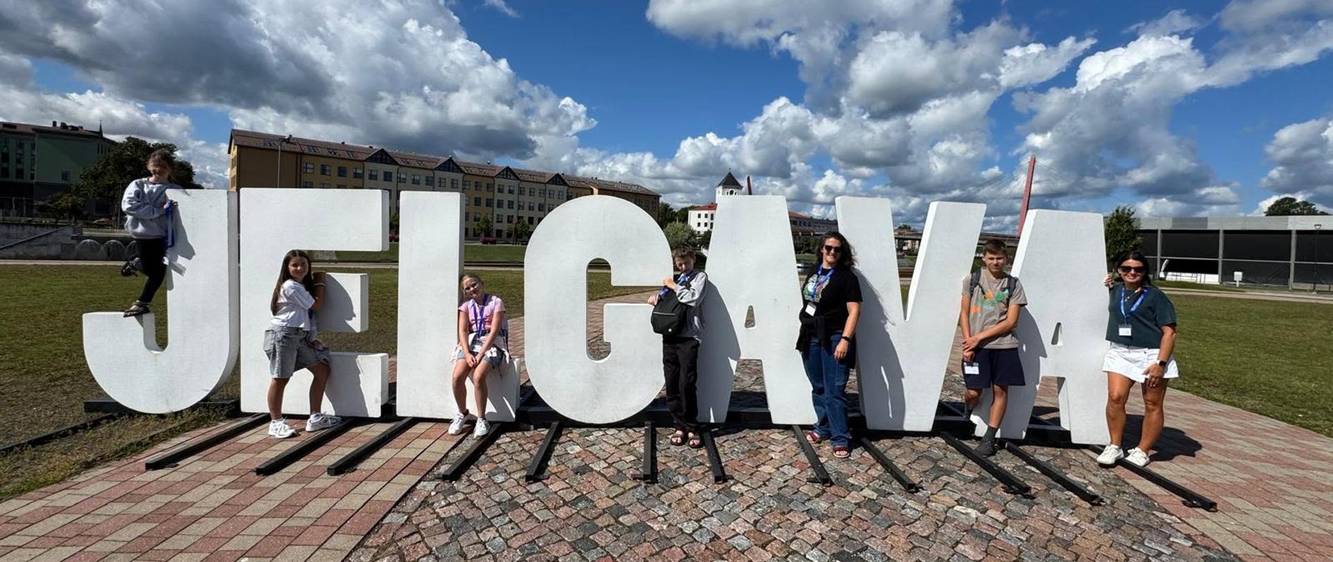 Zdjęcie pokazujące uczniów przed białym napisem Jelgava