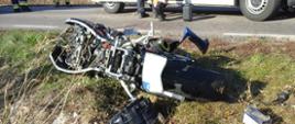 Uszkodzony motocykl po zderzeniu z samochodem osobowym leżący na poboczu jezdni. W motocyklu brak przedniego koło i kierownicy.