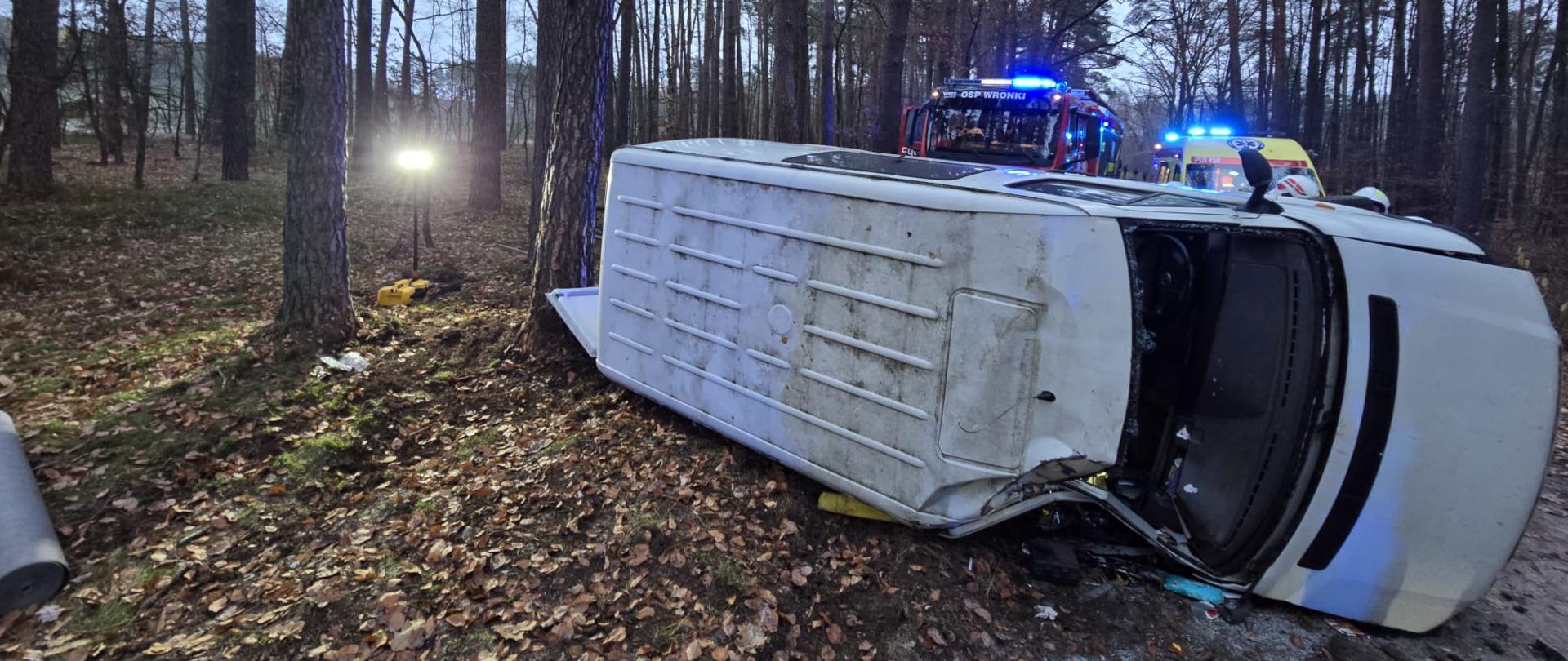 Samochód na boku przy drzewie, w pobliżu strażacy