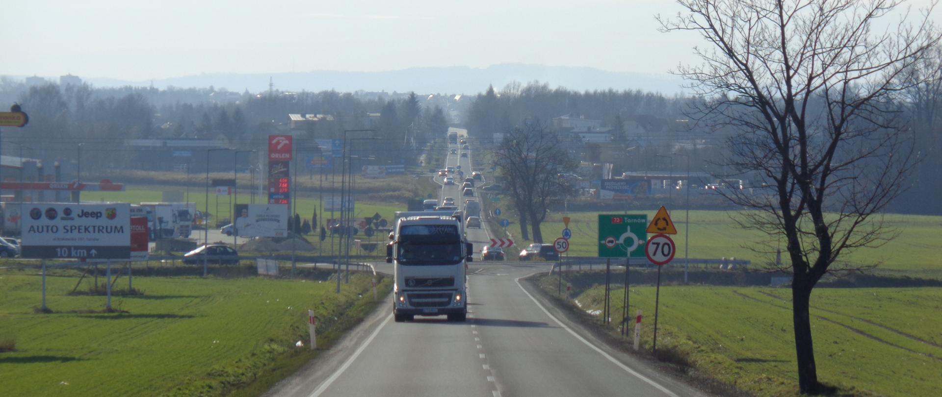 Jedna jezdnia po jednym pasie ruchu w każdym kierunku. Widoczne rondo z oznakowaniem na DK73 w kierunku Tarnowa. Po lewej stronie stacja benzynowa.