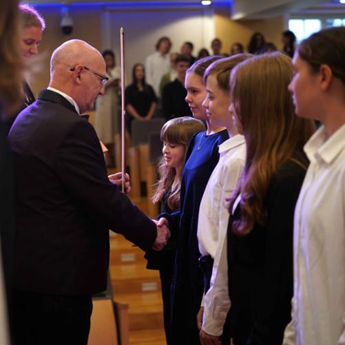 Zdjęcie przedstawia dyrektora szkoły podczas pasowania uczniów na scenie sali koncertowej, inne ujęcie