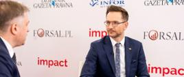 Minister rozwoju i technologii Waldemar Buda udzielający wywiadu podczas Impact'22, za plecami ministra baner z Impact'22 i logo Dziennik Gazeta Prawna