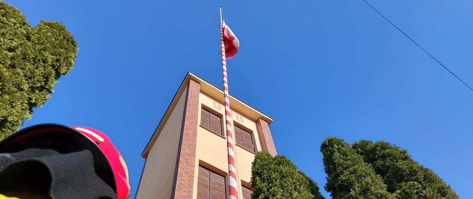 Zdjęcie przedstawia uroczyste podniesienie flagi Państwowej z okazji Święta Niepodległości. Na zdjęciu widzimy funkcjonariusz Państwowej Straży Pożarnej w Ostrzeszowie podczas upamiętnienia Święta Niepodległości. Zdjęcie wykonane w porze dziennej przed budynkiem Komendy.