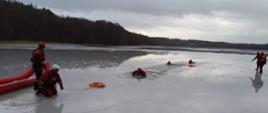 Trzech strażaków w specjalistycznym sprzęcie jest w wodzie czterech funkcjonariuszy Państwowej Straży Pożarnej ćwiczy pomoc.