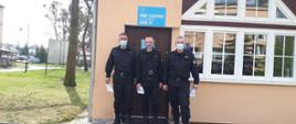 Przed wejściem do Punktu szczepień przeciw COVI-19 stoi trzech funkcjonariuszy Komendy Powiatowej Państwowej Staży Pożarnej w Świeciu w umundurowaniu dowódczo-sztabowym. W dłoniach trzymają kartki papieru. 